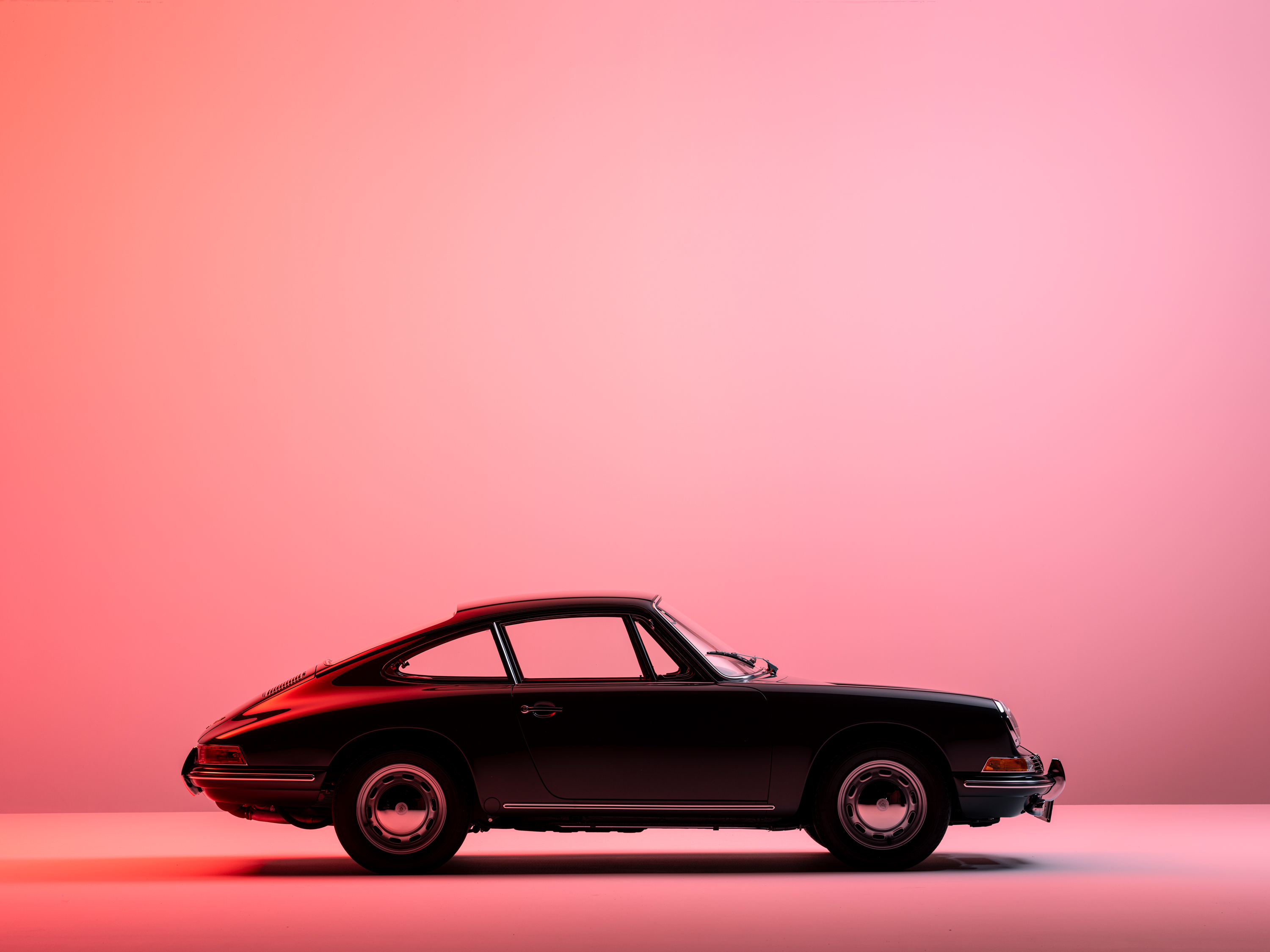 A black classic Porsche 911 against a coral backdrop